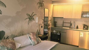 Een kleine hotelkamer met een bed, een kitchenette, een magnetron en een koelkast.