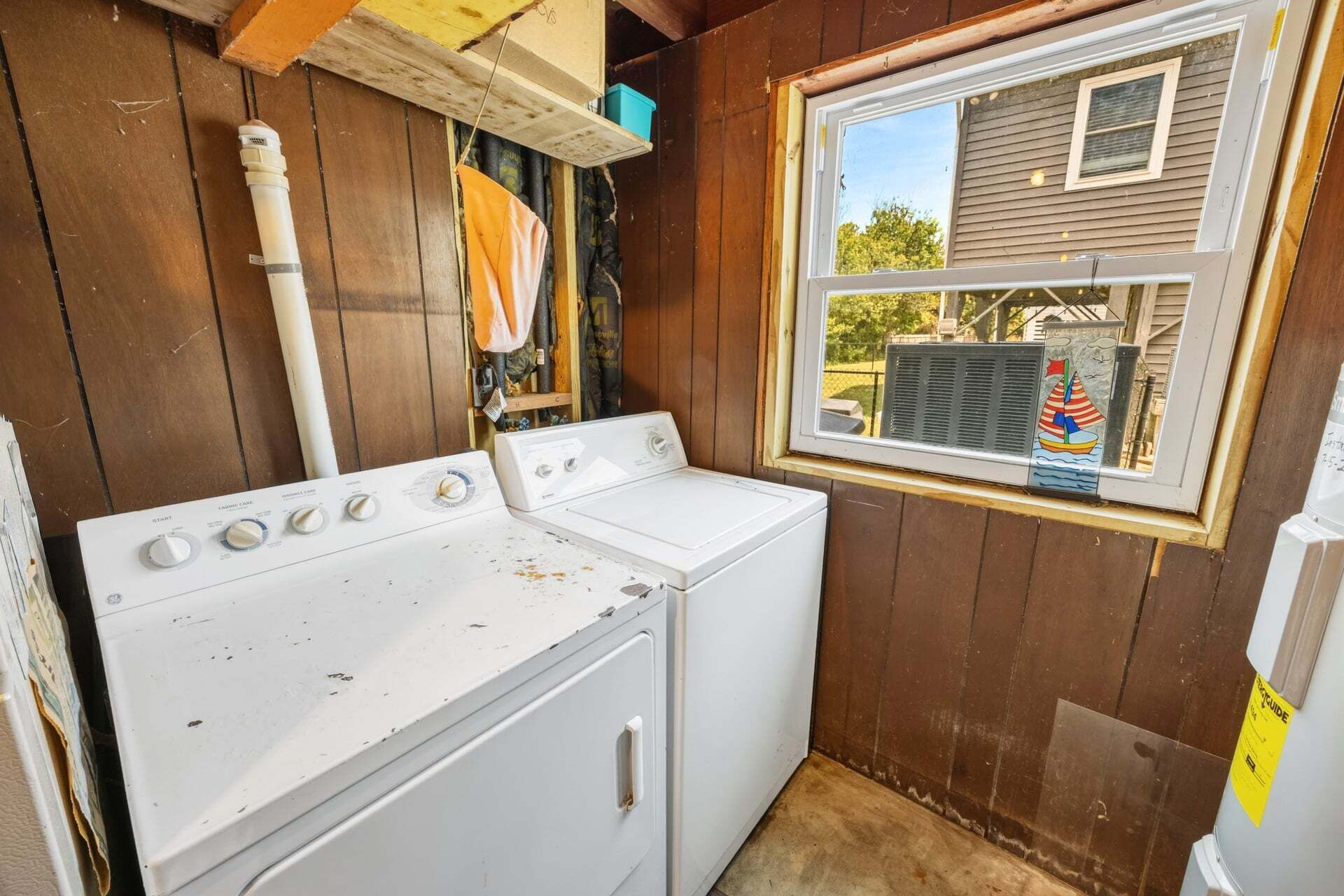 A laundry room with a washer and dryer, a window with a view of a house, and a vent hood above the dryer.