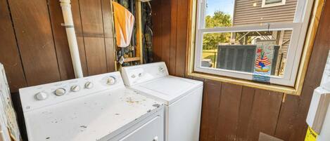 A laundry room with a washer and dryer, a window with a view of a house, and a vent hood above the dryer.