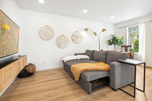 A modern living room with a grey sofa, a small table, a TV on a wooden cabinet, and wall art.