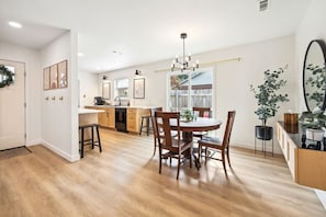 A modern kitchen with a dining area, wooden flooring, and a chandelier.