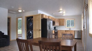 A compact kitchen with wooden cabinets, a built-in washer and dryer, and a dining area with a table and chairs. - The Cabins at Riptide Resort (Seward)