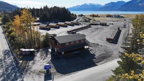 A large building with multiple rooms, a parking area, and a view of mountains and a lake. - The Cabins at Riptide Resort (Seward)