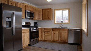 A kitchen with wooden cabinets, stainless steel appliances, a microwave, a stove, and a sink. - The Cabins at Riptide Resort (Seward)