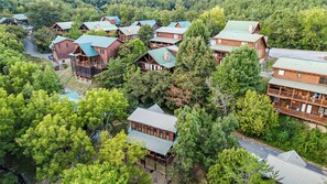 A cluster of log cabins with green roofs, surrounded by dense forest. - Couples Creekside Retreat w/ Hot Tub Near PF (Pigeon Forge)