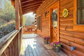 Une cabane en bois avec une véranda, une porte ornée d’une guirlande décorative et des pots de fleurs.