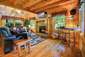 Un intérieur de chalet chaleureux avec une cheminée, un plancher en bois, un canapé, un téléviseur et un coin bar.