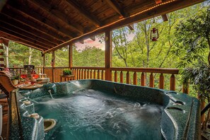 A hot tub with a wooden deck and railing, surrounded by lush greenery. - Couples Creekside Retreat w/ Hot Tub Near PF (Pigeon Forge)