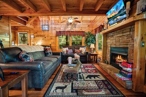 A cozy log cabin interior with a fireplace, leather sofas, and a television. - Couples Creekside Retreat w/ Hot Tub Near PF (Pigeon Forge)