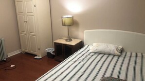 Une chambre à coucher comprenant un lit, une table de chevet, une lampe, une armoire et un radiateur.