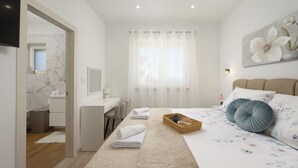 Une chambre à coucher comprenant un lit, un bureau, une chaise, un téléviseur et une fenêtre avec des rideaux.