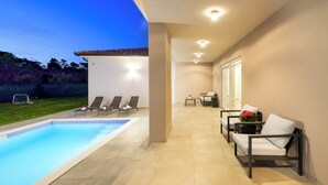 Une piscine avec des chaises longues, une petite table agrémentée d’une plante et un espace patio offrant une vue sur le jardin arrière.