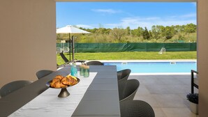 Un espace extérieur aménagé pour les repas, avec une table, des chaises et une vue sur une piscine.