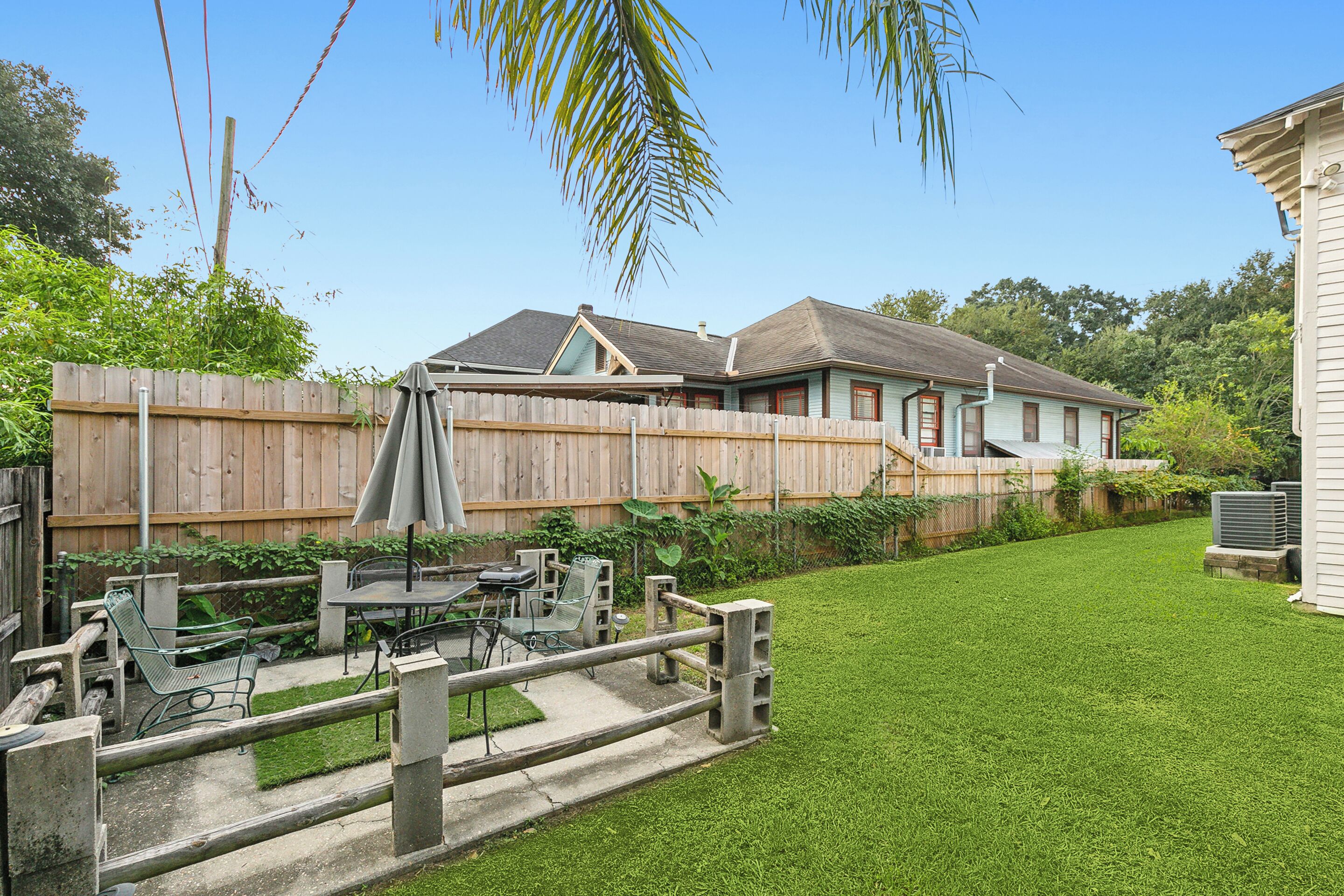 A backyard with a wooden fence, a patio with outdoor furniture, and a house with a gabled roof.