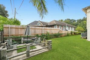 Un jardin avec une clôture en bois, une terrasse avec des meubles d’extérieur et une maison avec un toit à pignon.