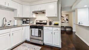 A modern kitchen with white cabinetry, stainless steel appliances, and a granite countertop. - Spacious 3-Bedroom Uptown House – Steps to Streetcar & Downtown (New Orleans)