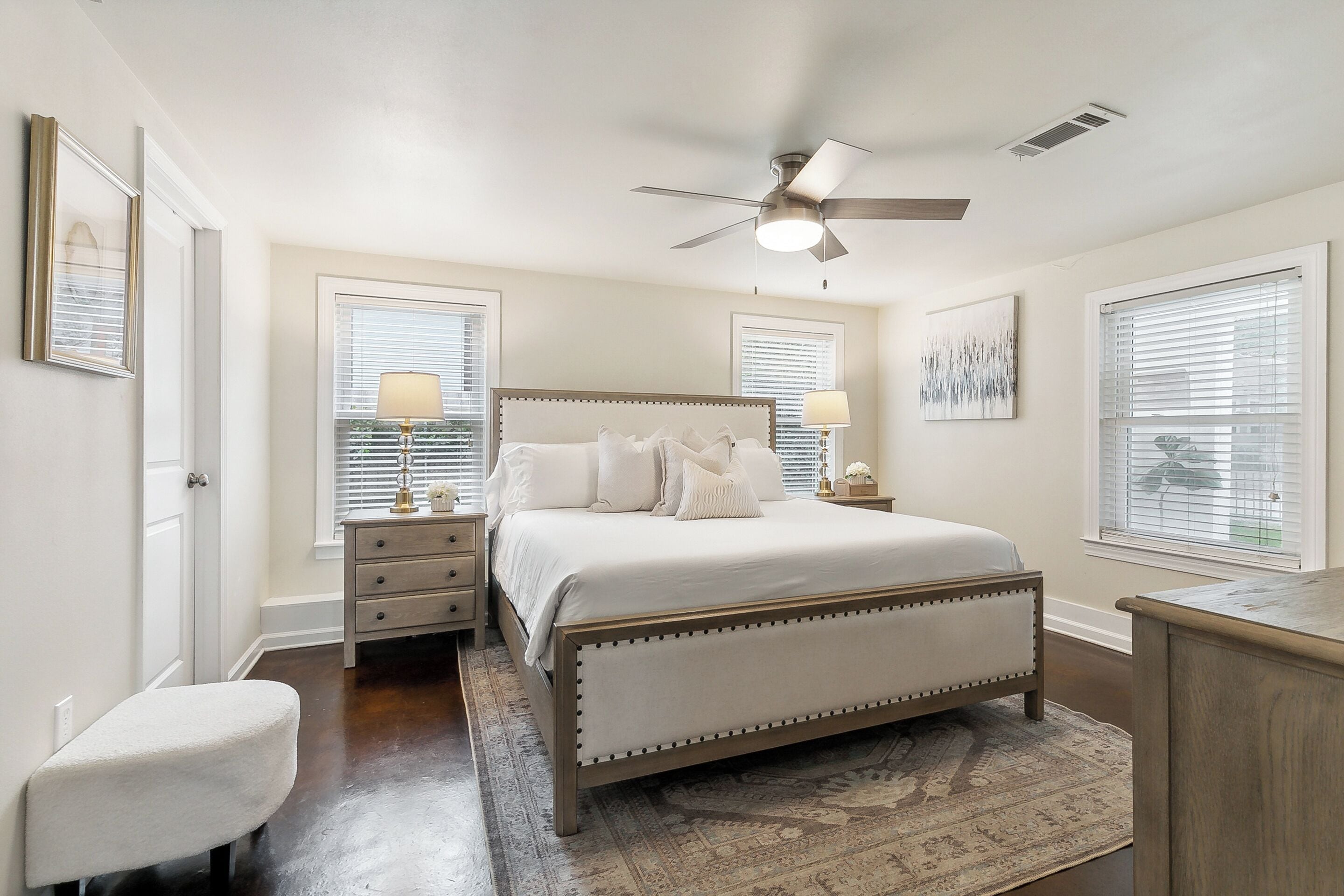 A bedroom with a bed, bedside tables, a chair, a ceiling fan, and a window with blinds.