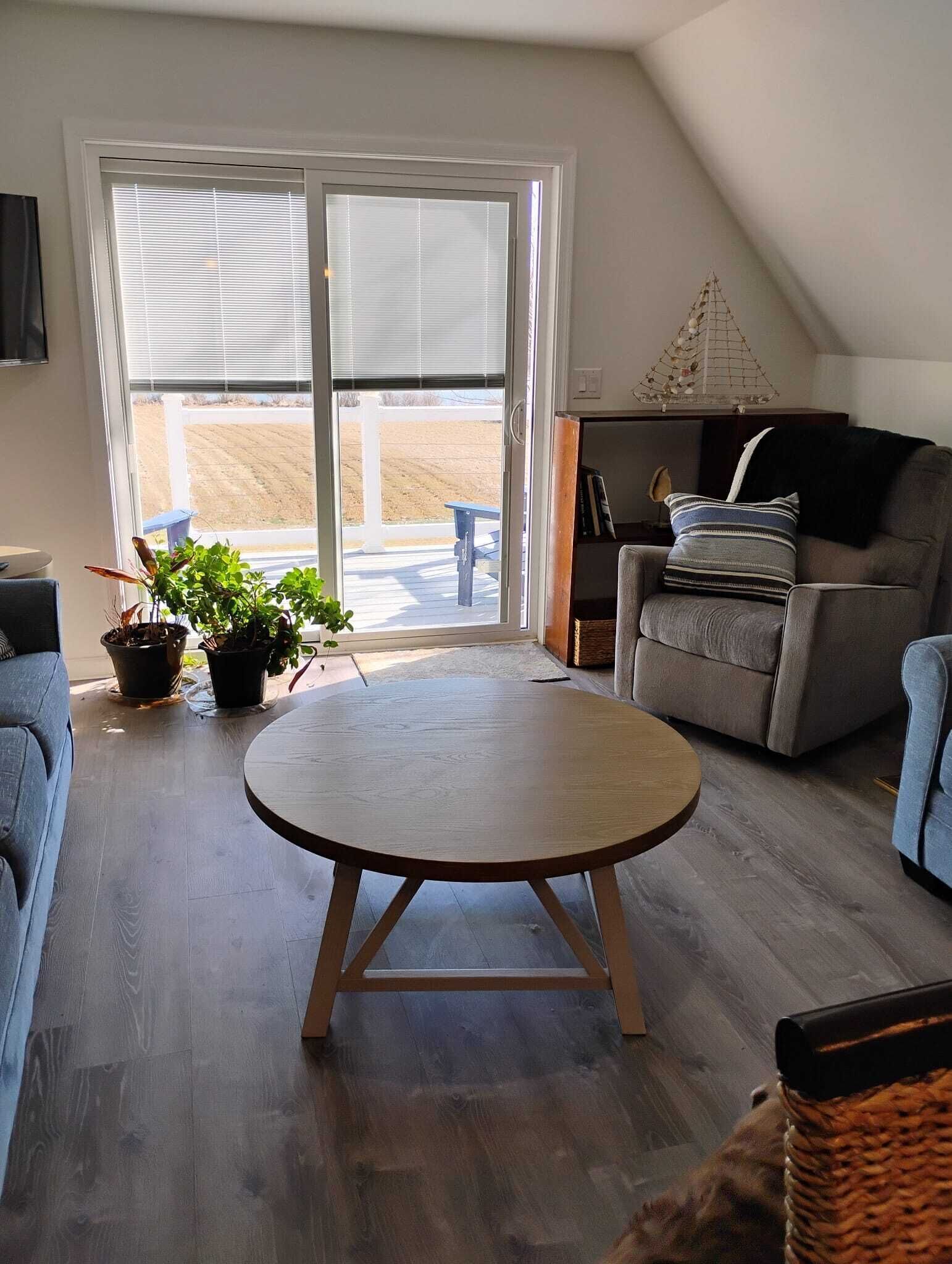 A living room with a round wooden table, a sofa, a chair, and a bookshelf.