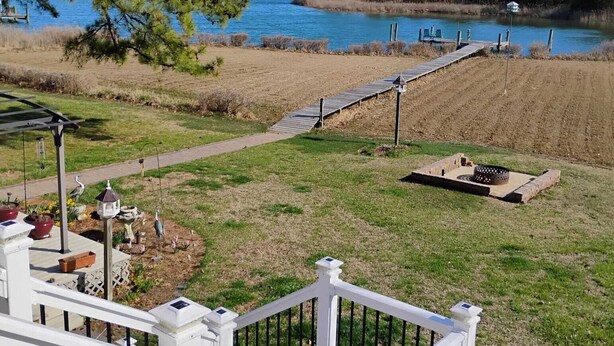 A deck with a railing overlooking a lake, a pathway leading to the water, and a small garden area with potted plants. - Quiet Waterfront Getaway Private Escape 1BR Apt Retreat with Optional Boat Dock (Stevensville)