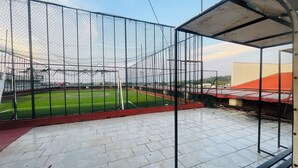 Un campo deportivo rodeado por una cerca de alambre, con suelo de baldosas y un banco.