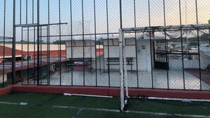Un campo deportivo cercado con un arco cubierto por una red, rodeado de edificios y un cielo despejado.
