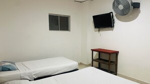 Una habitación con dos camas, ventana, televisión y ventilador.
