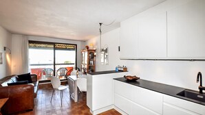 A modern kitchen with white cabinets, a black countertop, and a dining area with a wooden table and chairs. - Lovely home in Le Barcarès with lake view (Le Barcarès)