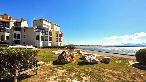A hotel with a large building, a grassy area with rocks, and a view of the sea. - Lovely home in Le Barcarès with lake view (Le Barcarès)