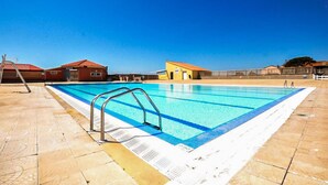 A swimming pool with a diving board, a lifeguard stand, and a small yellow building in the background. - Lovely home in Le Barcarès with lake view (Le Barcarès)