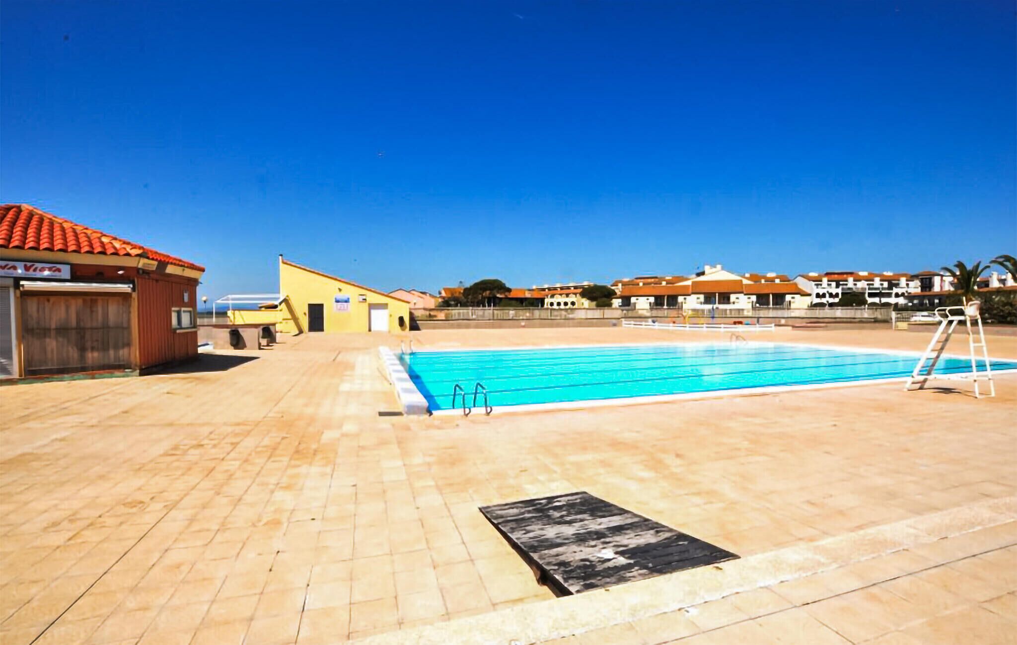 A swimming pool with a diving board, a covered area with a door, and a building with a red roof.