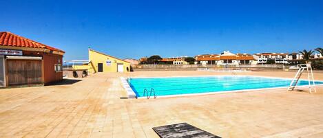 A swimming pool with a diving board, a covered area with a door, and a building with a red roof.
