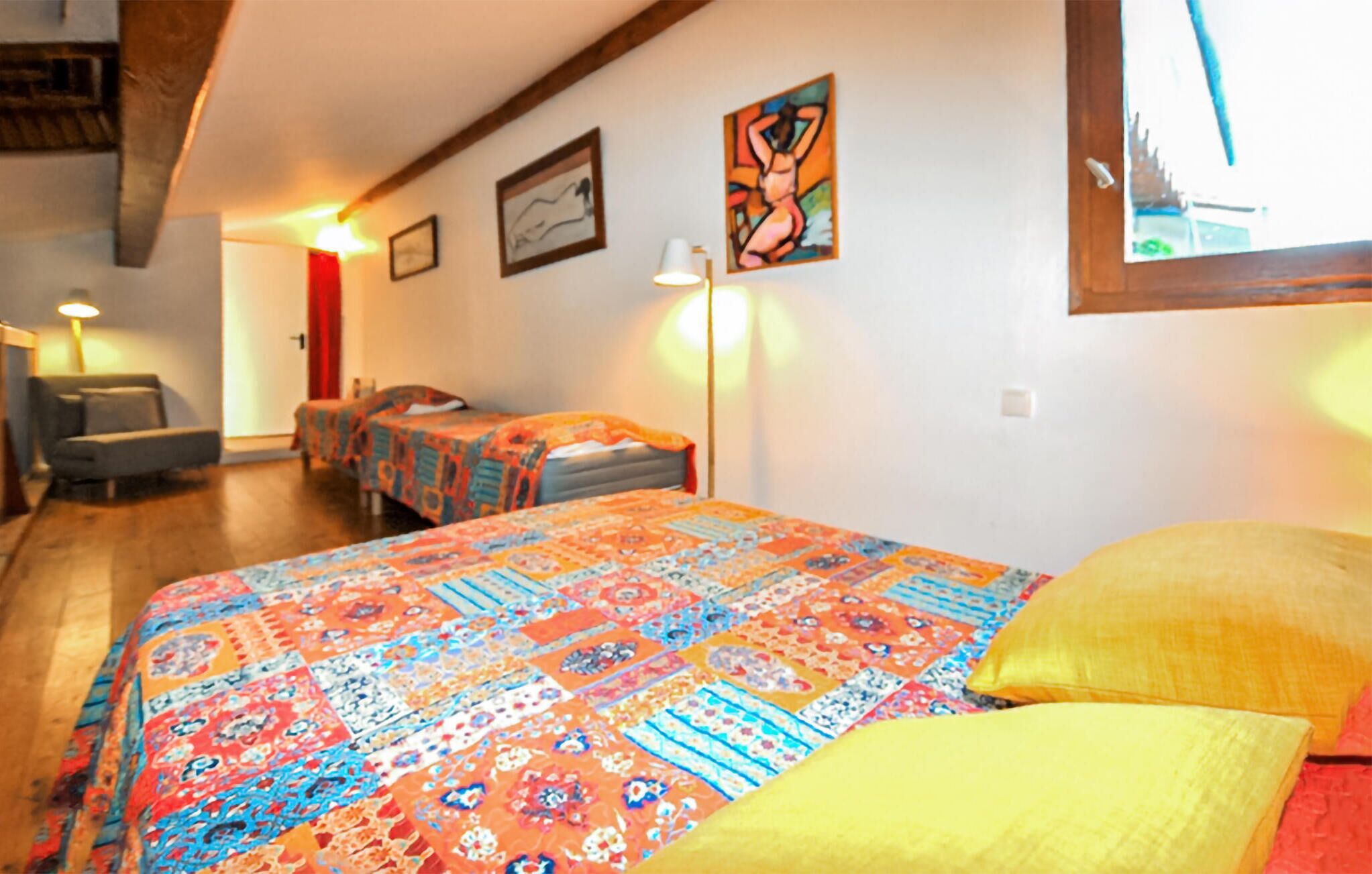 A room with a large bed, two smaller beds, a chair, and a desk.