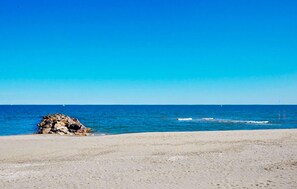 Een strand met een rotsformatie en een helderblauwe lucht.