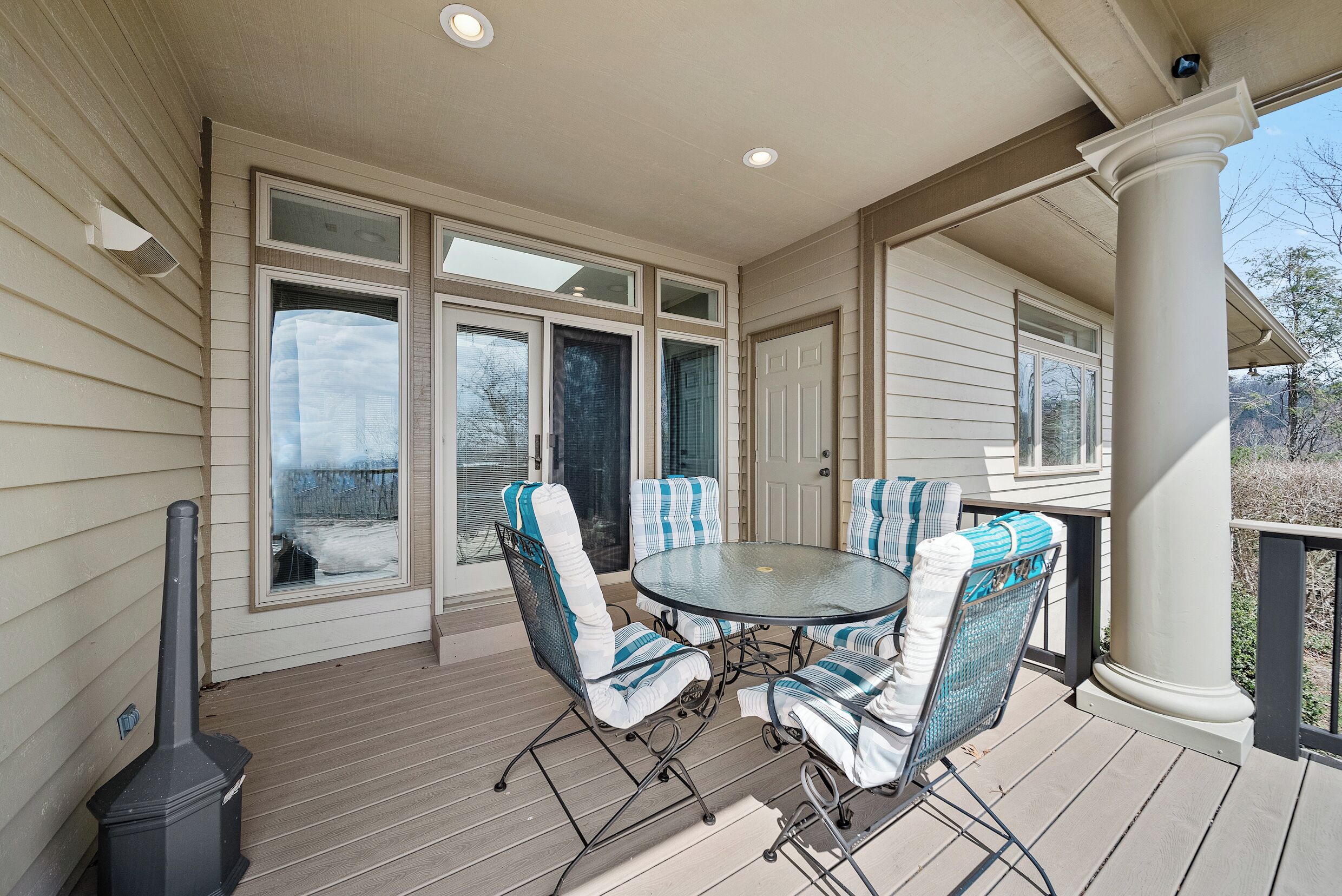 A covered patio with a round table and six chairs, a grill, and large windows.