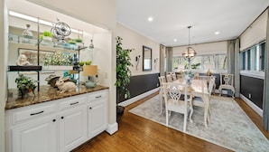 A kitchen with white cabinets, a granite countertop, and a dining area with a table and chairs. - Panoramic Blue Ridge Views | Expansive Deck, Fireplace, One-Level Living (Blowing Rock)