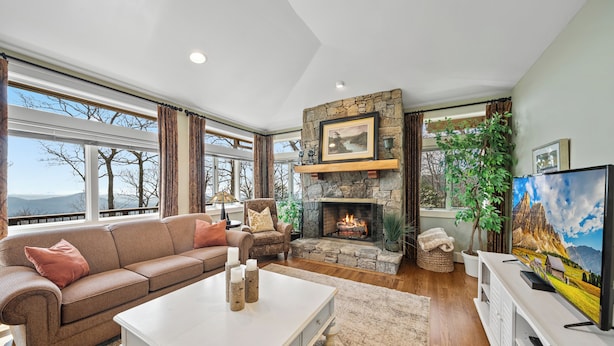 A living room with a stone fireplace, a sofa, a coffee table, and a television. - Panoramic Blue Ridge Views | Expansive Deck, Fireplace, One-Level Living (Blowing Rock)
