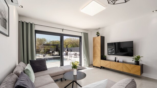 Ett modernt vardagsrum med en soffa, ett soffbord, en tv och utsikt över en uteplats.