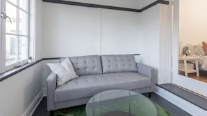 Ein Zimmer mit einer grauen Couch, einem Glastisch und einem Fenster.