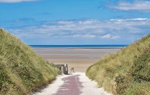Ein Weg, der zu einem Strand mit Dünen an beiden Seiten führt.