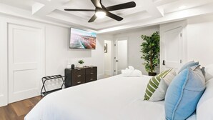A bedroom with a bed, a ceiling fan, a TV, a plant, and a door. - Eternity Wellness Retreat Jacuzzi/Sauna/ColdPlunge (Tampa)