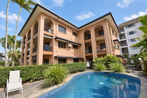 Ein mehrstöckiges Hotel mit Swimmingpool, umgeben von Palmen und viel Grün.