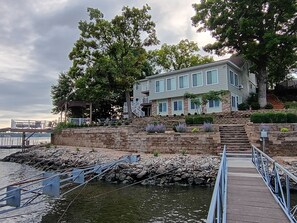 Ein Anwesen am Wasserufer mit einem Steg, Steinstufen, die zu einem Haus führen, und Blick auf das Wasser.