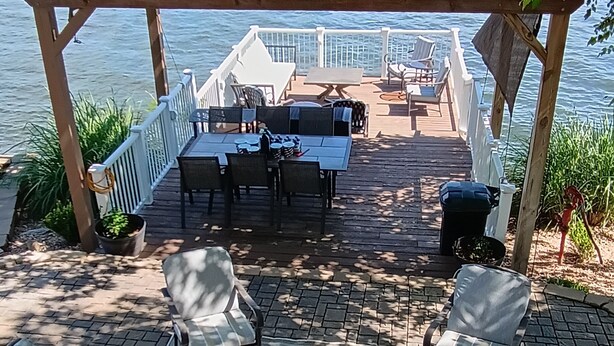En træterrasse med udendørs møbler, en pergola og udsigt til vandet.