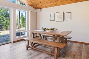 A wooden dining table with benches, a window with curtains, and three framed pictures on the wall.