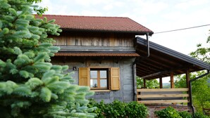 Ein rustikales Holzhaus mit Ziegeldach, einer Holzveranda und einem Fenster mit Rollläden.