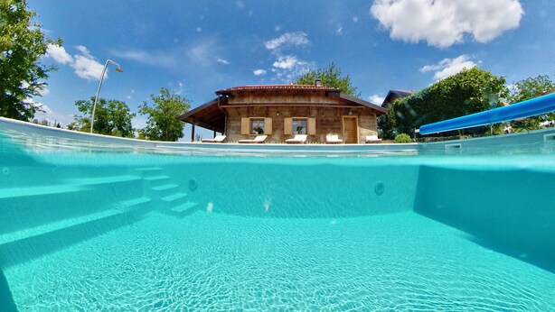 Ein klares Schwimmbecken mit Blick auf ein Gebäude mit einem geneigten Dach und Fenstern.