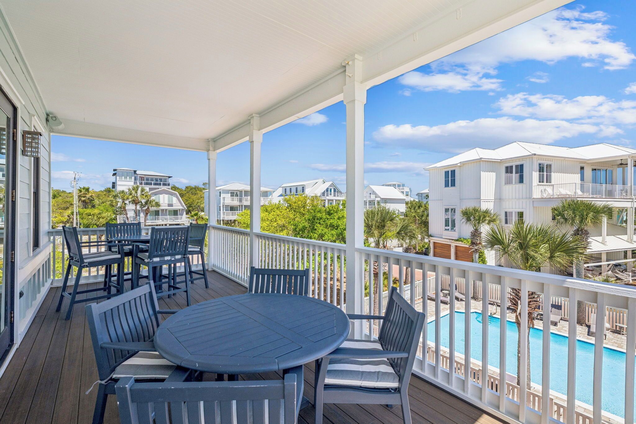 A covered outdoor deck with a pool, dining area, and white railings.