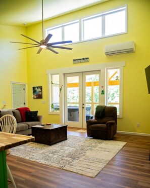 A living room with a ceiling fan, a large window, and a sliding glass door leading to an outdoor area.