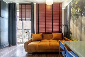 Ein stilvolles Wohnzimmer mit einer Couch, einem Glastisch und Blick auf eine Stadtlandschaft durch große Fenster.