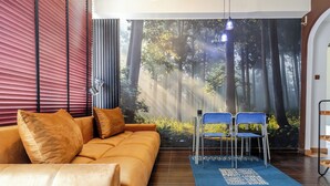 Moderni olohuone, jossa on sohva, kaksi nojatuolia, sininen matto ja seinällä metsäaiheinen seinämaalaus.